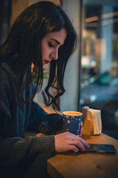 Young Woman Enjoying Coffee and Browsing Smartphone in a Cozy Cafe