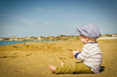 Adorable Baby in Striped Cap Playing with Sand on Sunny Beach image