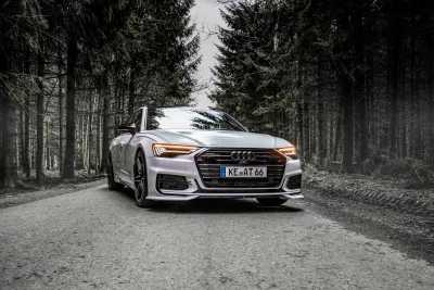 Sleek White Audi Automobile Amidst Desaturated Forest Scenery with Bright Headlights image
