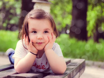 Cute Toddler Girl Resting Chin on Hands on Rustic Park Bench image