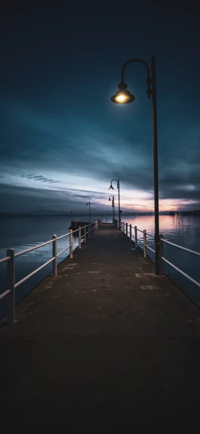 Tranquil illuminated pier at twilight with dramatic sky reflecting on calm water image