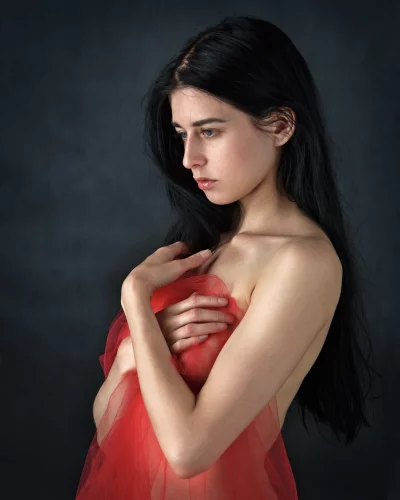 Pensive Young Woman in Red Sheer Fabric with Downcast Gaze image