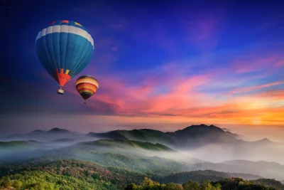 Colorful Hot Air Balloons Soaring Over Misty Mountain Landscape at Sunset image