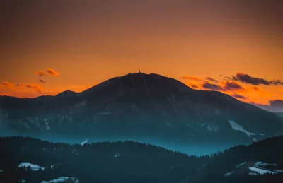 Majestic Mountain Peaks at Golden Hour with a Glowing Orange Sky and Atmospheric Mist image