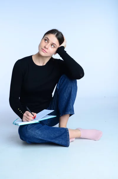 Pensive Young Woman Writing Notes in Notebook on White Background image