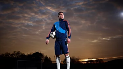 Professional Soccer Player Posing with Ball Under Dramatic Sunset Sky image