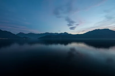 Serene Mountain Lake Reflection at Twilight with Soft Pastel Clouds and Distant City Lights image