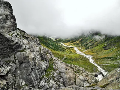 Dramatic Alpine Valley with Glacial River Flowing Through Misty Mountain Landscape image