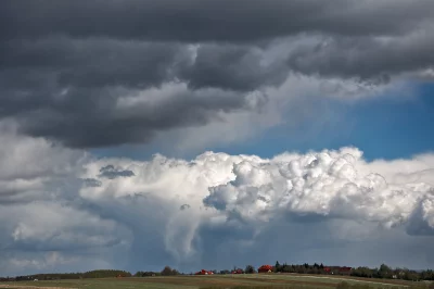 Dramatic Storm Clouds Gathering Over Rural Landscape with Distant Houses and Blue Sky image