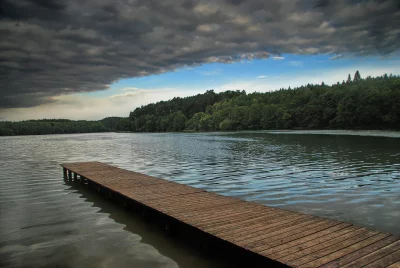 Rustic Wooden Pier on a Tranquil Lake Under Dramatic Cloudy Sky and Forest image