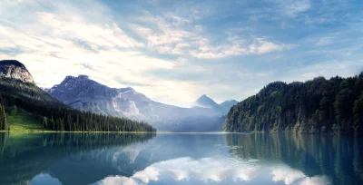 Serene Mountain Lake Reflecting Majestic Peaks and Forest Under Dynamic Cloudy Sky image