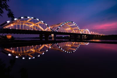 Illuminated Arch Bridge Reflecting on Calm River at Twilight image