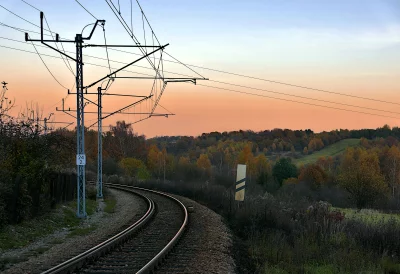 Scenic Railway Track Curving Through Autumn Landscape at Sunset with Overhead Lines Wallpaper image