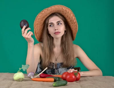 Thoughtful Woman in Straw Hat Holding Avocado with Garden Vegetables image