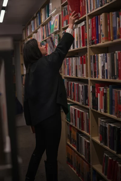 Young Woman Reaching for a Red Book on a Bookshelf in a Bookstore