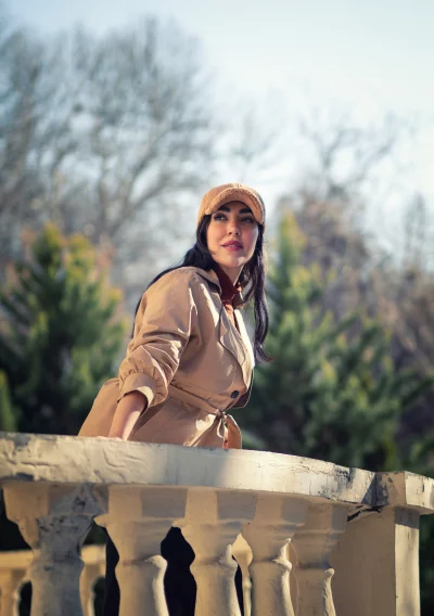 Stylish Woman in Trench Coat on Balcony Overlooking Trees