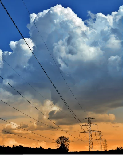 Dramatic Sky with Towering Clouds Over Power Lines and Silhouetted Landscape at Dusk image