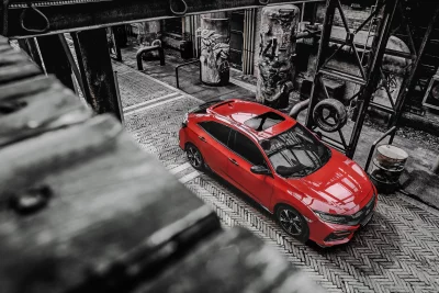 Vibrant Red Hatchback Against Gritty Industrial Urban Background image