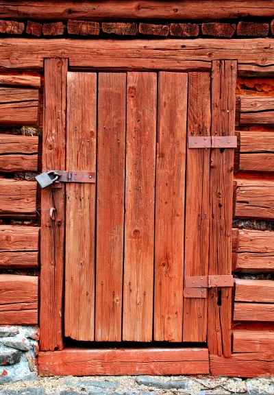 Rustic Weathered Red Wooden Door with Padlock on an Old Log Cabin Wall image