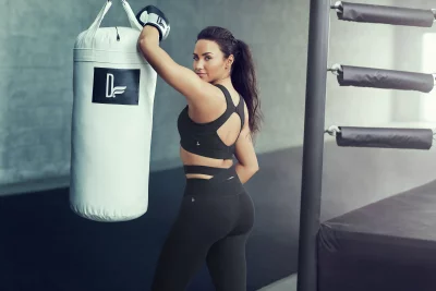 Confident Woman in Athletic Wear and Boxing Gloves Posing with Punching Bag in Gym image