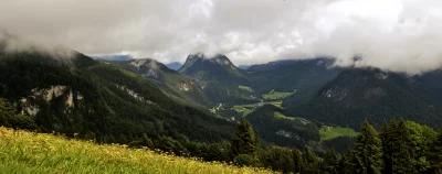 Panoramic Alpine Valley with Village Amidst Cloudy Forested Mountains image