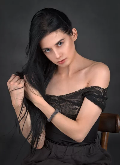 Pensive Young Woman Gently Pulling Long Black Hair in Black Lace Top image