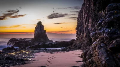 Vibrant Coastal Sunset Over Rugged Sea Stack and Serene Beach with Footprints image