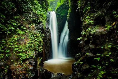 Serene Waterfall Cascading into Muddy Pool Amidst Dark Jungle Rocks with Lush Greenery image
