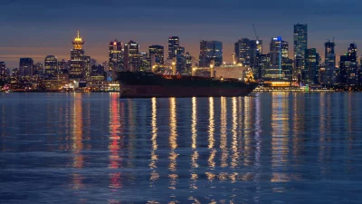 Industrial Cargo Ship Passing a Vibrant Illuminated City Skyline at Tranquil Dusk image