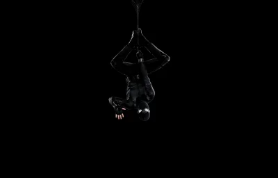 Stealthy Superhero in Black Tactical Suit Hanging Upside Down Against Dark Background image