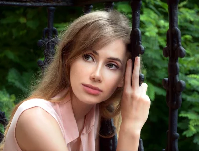 Pensive Young Woman with Blonde Hair Leaning on Ornate Iron Fence image