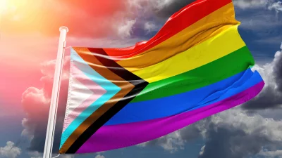 Vibrant Progress Pride Flag Waving Against Dramatic Sky with Radiant Sun Flare image