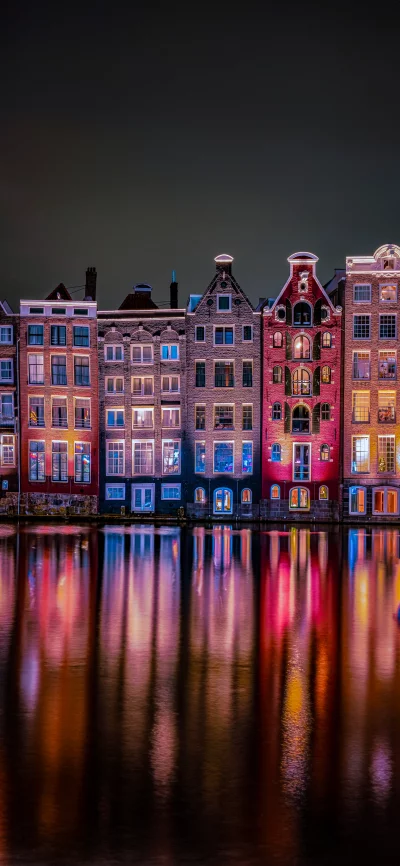 Illuminated Amsterdam Canal Houses at Night with Water Reflections