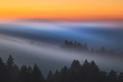 Misty Mountain Forest Landscape at Dawn with Vibrant Orange Sky and Ethereal Fog image