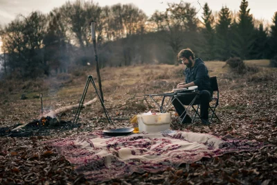 Solo Traveler Prepares Outdoor Dinner Over Campfire in Rustic Wilderness at Dusk