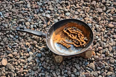Corroded Bicycle Chain Resting in Vintage Frying Pan on Outdoor Gravel Surface image