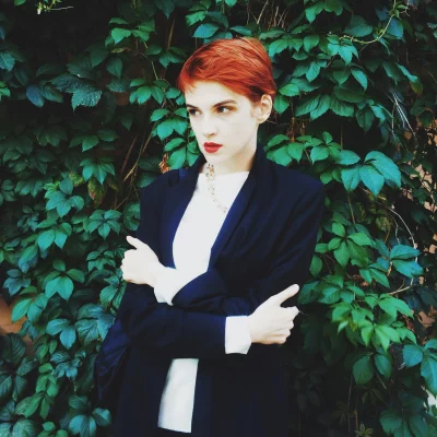 Stylish Red-Haired Woman in Blazer Posing Confidently Against Green Foliage