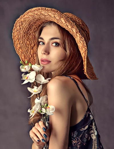 Graceful Young Woman in Straw Hat Holding Delicate White Orchids image