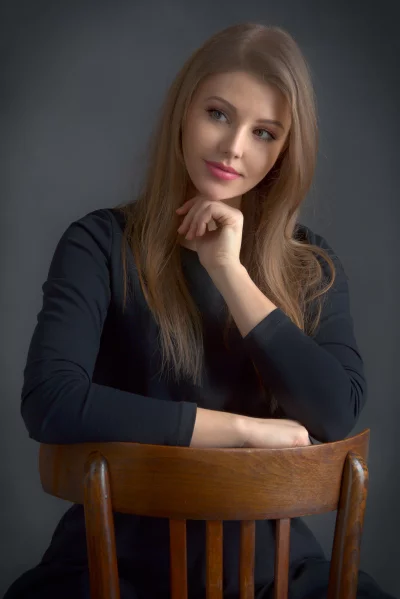 Elegant Young Woman with Long Blonde Hair Posing Thoughtfully on Wooden Chair image