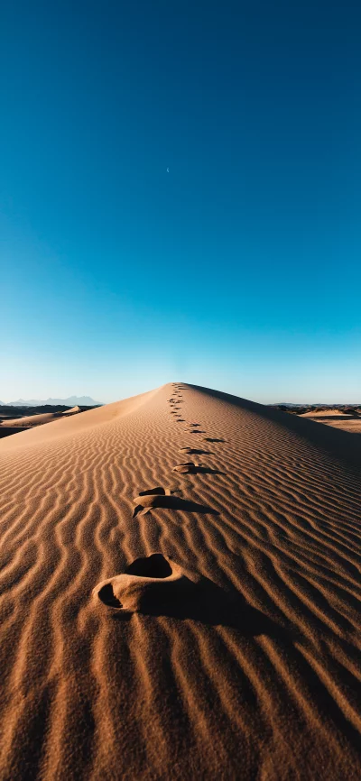 Footprints on a windswept sand dune under a clear blue sky