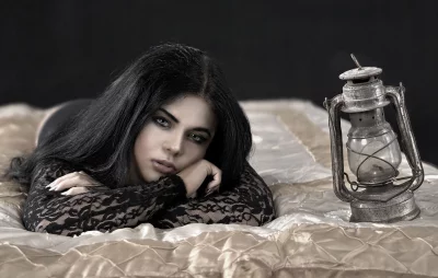 Pensive Woman with Long Dark Hair and Vintage Lantern on Elegant Bed image