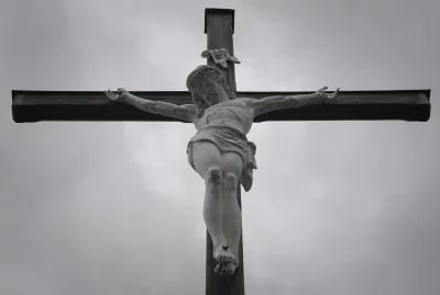 Solemn White Christ Statue on Rustic Wooden Cross Against Overcast Sky image