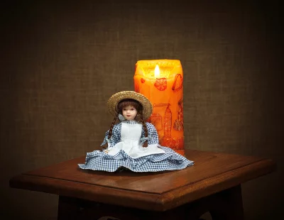 Vintage Doll with Straw Hat Beside Glowing Orange Candle on Wooden Table image
