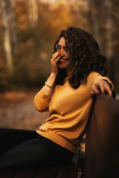 Cheerful brunette curly hair woman smiling in a park with fall foliage and smileing